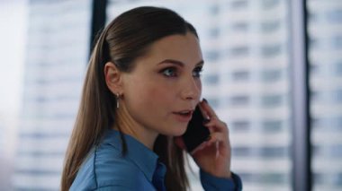 Güzel bir çalışan panoramik pencereye yakın mesafeden cep telefonunu arıyor. Modern ofis alanında akıllı telefondan konuşan genç bir iş kadını portresi. Kendine güvenen girişimci iş telefonuyla konuşuyor.