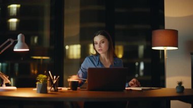 Çevrimiçi proje üzerinde çalışan fazla mesai çalışanları not defterine notlar yazıyorlar. Ciddi bir iş kadını gece vardiyasında fazla mesai yapıyor. Girişimci kadın karanlık ofiste kahve içerek işe başlıyor.