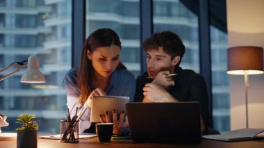 Kadın koç, karanlık işyerindeki tablet verilerini göstererek çalışanlara iş konusunda yardım ediyor. Dost canlısı iş arkadaşları gece geç saatlerde projeyi tartışıyorlar. Gülümseyen bayan patron günlük işlerde yönetici asistanı..