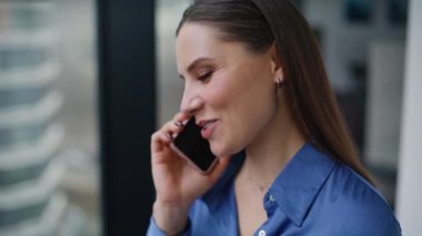 Portre işkadını cep telefonunu arıyor. Dostça sohbetin tadını çıkarın. Güzel, gülümseyen bir kadın ofis penceresinin önünde akıllı telefondan konuşuyor. Cep telefonuyla yakın çekimle lüks esmer kadın paylaşım haberleri.