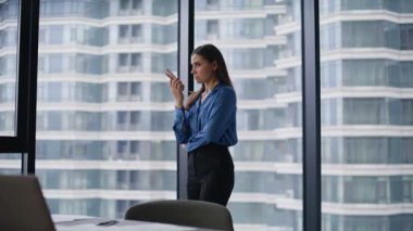 Girişimci ofis panoramik penceresinde cep telefonu hoparlörüyle konuşuyor. Kendine güvenen kadın yönetici akıllı telefondan sesli mesaj kaydediyor. İş kadını cep telefonuyla iş görevlerini dikte ediyor.
