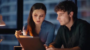 İki yönetici karanlık ofisteki tablet verilerini analiz ediyor. Profesyonel yöneticiler internet üzerinden iş birliği yapıyor. Şirket gelişimini tartışan çalışkan ortaklar..