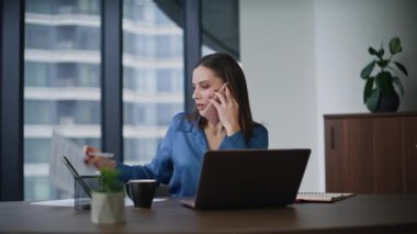 İş kadınını arayıp şirket işyerindeki belgeleri kontrol ediyorum. Gülümseyen kadın ofis müdürü cep telefonuyla sözleşme detaylarını tartışıyor. Gülen bayan patron modern çalışma alanında akıllı telefondan bahsediyor.