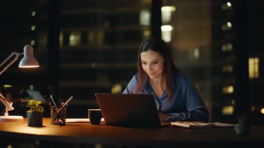 Kadın serbest çalışan, gece ofisindeki web kamerası laptopuyla konuşuyor. Gülümseyen iş kadını bilgisayar kapağını lamba ışığında kapatmayı bitirdi. Mutlu son yöneticiler başarılı online pazarlıklardan memnun.