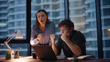 Şaşırtıcı iş adamları zafere seviniyor. Akşam ofiste dizüstü bilgisayar izliyorlar. Aşırı mutlu meslektaşlar duygusal olarak başarıya tepki veriyor. İki mutlu iş arkadaşı beşli takım çalışmasının keyfini çıkarıyor..