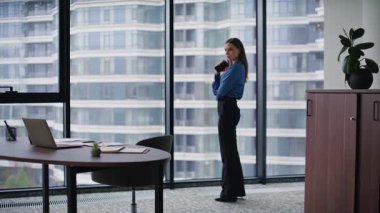 Düşünceli iş kadını elinde cep telefonuyla panoramik pencereye bakıyor. Modern ofis işini düşünen zarif bir kadın CEO. Şirketin iş yerinde sakin, esmer görünümlü akıllı telefon..