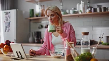 Çevrimiçi kız kahve içiyor, tablet izliyor, apartman mutfağını kapatıyor. Evde kahvaltı yaparken bilgisayarında haber okuyan sarışın bir kadın var. Gülümseyen serbest çalışan mutlu bir sabah geçiriyor. 