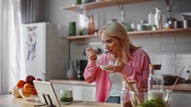 Serbest çalışan, mısır gevreği yiyor mutfak tezgahında tablet ekranına bakıyor. Evde rahat bir kadın sabah rutininin tadını çıkarıyor. Sakin kız dijital aygıtla sosyal medyayı izliyor 