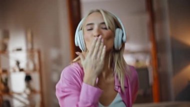 Müzik aşığı, ev portresindeki favori şarkıyı dinlerken kamerayla etkileşime giriyor. Kablosuz kulaklıklarla el kol hareketi yapan dansçı kadın. Müzikten hoşlanan oyuncu bayan ritme ayak uyduruyor. Enerjik kız eğleniyor.