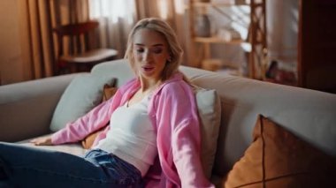 Sarışın manken eve yakın çekimde koltuğa oturuyor. Dümdüz iç mekanda rahat bir dinlenme kanepemiz var. Rahat bir kadın, rahat bir dairede kaygısızca uzanmış yastıklar hissediyor. Bayan dinleniyor.