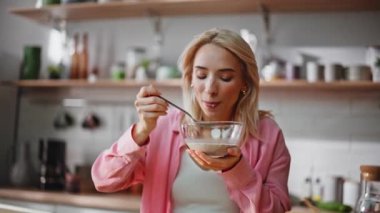 Sabah sarışını kahvaltısını yapıyor. Mutfaktaki tablette müzik dinliyor. Gülümseyen pozitif bayan, evde oturup, ellerinde tabakla dans ediyor. Mutlu kadın arayan pad bilgisayar içeriği 