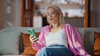 Modern oturma odasında çok çalışan bir kadın kanepeye düşüyor. Rahat kız, akıllı telefon kullanarak kanepede uzanıyor. Sarışın bayan hafta sonları huzurlu vakit geçiriyor. Kaygısız kadın rahatça dinleniyor. 