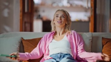 Evde elinde cep telefonuyla koltuğa düşen sarışın kadın. Kaygısız neşeli kız hafif oturma odasında dinleniyor. Tatmin olmuş bir kadın rahat bir apartman dairesinde rahat rahat cep telefonuna bakıyor.