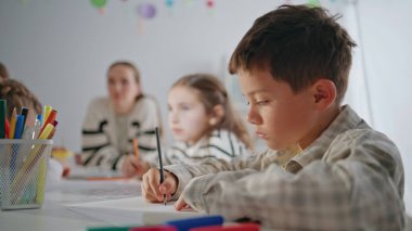 Çalışkan öğrenci sınıfta kurşun kalem çiziyor. Yakın plan. Odaklanmış çocuk oditoryumda sınıf arkadaşlarıyla resim yaratıyor. Ciddi çocuk resim dersinden zevk alıyor. Konsantre oluyor. Yaratıcılık kavramı