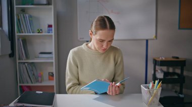 Sakin eğitimci sınıfta ev ödevlerini kontrol ederken yaptığı hataları düzeltiyor. İş yerinde elinde defter okuma sınavı olan genç bir kadın. Okulda çalışan ciddi bir öğretmen. Meslek kavramı