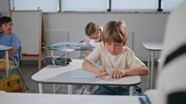 Okul çocuğu sınıfın masasında oturuyor. Yakın plan. Sınıfta ciddi öğrenci dinleme dersi çözme sınavı. Masada not defteri yazan zeki bir öğrenci. Oditoryumda sınıf arkadaşlarıyla çocuk eğitimi. 