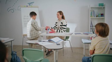 Çocuk hafif sınıfta beyaz tahta yazarak sınıf çalışması yapıyor. Masadaki çocuklara ders veren kadın öğretmen. Doğru cevabı veren mutlu öğrenci. Zeki çocuklar ilkokulda eğitim alıyorlar. 
