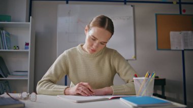 Ödevleri kontrol eden özenli öğretmen sınıftaki çalışma okulunu kapatıyor. Sakin kadın öğretmen, defter görünümlü. Sadece dolapta iz bırakıyor. Bayan eğitimci sınav sonuçlarını okuyup derse hazırlanıyor.