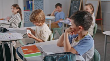 Sınıf arkadaşından komik bir çocuk notu okuyup yakın çekimde gülüyor. Okulda ders veren iki çocuk. Masalarda oturan sevimli öğrenciler. Meraklı çocuklar kabinede birbirleriyle iletişim kurarken eğleniyorlar.