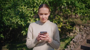 Sunny Park 'ta SMS okuyan genç bir kadın. Modern akıllı telefon kullanan çekici iş kadını yeşil doğada internette sörf yapıyor. Merdivenin yanında tek başına cep telefonu kullanan romantik bir kız.