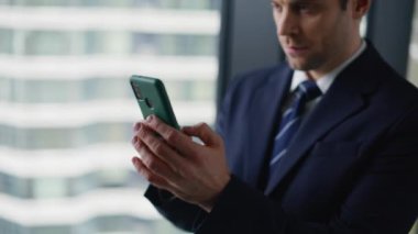 Zengin işadamı ofis penceresinin önünde cep telefonuna mesaj atıyor. Ciddi bir işletme yöneticisi kapalı alanda akıllı telefonla mesaj gönderiyor. Kendine güvenen yönetici çevrimiçi cep telefonu uygulaması.