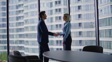 İş kadını ofis panoramik penceresinden selamlıyor. İş yerindeki resmi toplantıda kendine güvenen iki iş ortağı el sıkışıyor. Modern şirket içinde gülümseyen meslektaşlar el sıkışır..