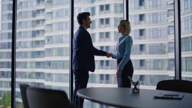 Kendine güvenen işadamı modern ofiste kadın yöneticiyle tokalaşıyor. Şirket ortakları iş görüşmeleri için toplanıyor. Profesyonel meslektaşlar panoramik kabine penceresinde bekliyorlar