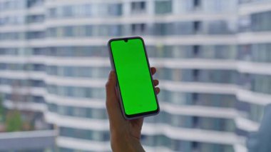 Model cep telefonundan alışveriş yapan bir bayan apartmanın penceresinin yanında duruyor. Yakınlaş. İş kadını yeşil ekran cep telefonuyla iş e-postası gönderiyor. Krom tuşlu akıllı telefondaki kadın mesajına göz at