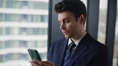 Gülümseyen girişimci vitrin iş merkezinin yanında duran SMS 'leri okuyor. İşte cep telefonundan sosyal medyayı izleyen başarılı bir iş adamı portresi. Lüks yönetici çevrimiçi telefon uygulamasına göz atın