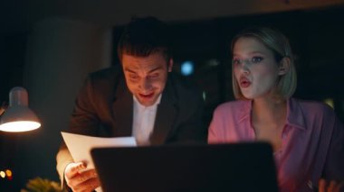 Başarılı girişimciler gece ofislerinde beş tatmin edici gelir sağlıyorlar. Gülümseyen iş adamları proje başarısının keyfini çıkarıyorlar. Dizüstü bilgisayara bakan iki iş arkadaşı akşam başarısını kutluyorlar.