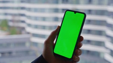 İş adamı, pencere kenarı manzaralı akıllı telefonu yakından takip ediyor. Tanımlanamayan yönetici yeşil ekran cep telefonu kullanarak internette sörf yapıyor. Girişimci tarama uygulaması kroma anahtar cep telefonu.