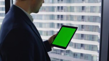 Girişimci iş merkezi penceresindeki kromakey tablet verilerini tarıyor ve yakınlaştırıyor. Başarılı iş adamı ofisteki yeşil ekranlı bilgisayarı izliyor. Yönetici içeride bir model düzeneği tutuyor.