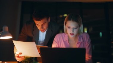 İki yönetici gece geç saatlerde iş yerinde dizüstü bilgisayarla birlikte çalışarak belgeleri tartışıyorlar. Ciddi meslektaşlarım evrakları inceliyor. Gece ofisinde iş stratejisi planlayan fazla mesai çalışanları.
