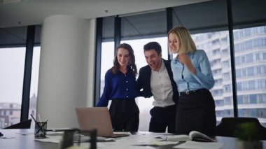 Aşırı sevinçli takım üyeleri birlikte zafere tepki veren dizüstü bilgisayara bakıyor. Mutlu iş arkadaşları ofisteki mutlu iş başarılarını kucaklıyor. Başarılı bir işbirliğinin keyfini çıkaran üç meslektaşın gülümsemesi.