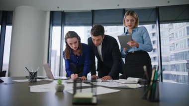 İş ekibi ofis masasında belgeleri birlikte inceliyor. Üç meslektaşı, iş yerinde beyin fırtınası yapan fikirleri değerlendirmek için kağıtları incelemeye teşvik etti. Toplantıda evrak işleri yapan profesyonel iş arkadaşları..