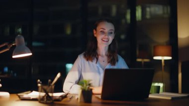 İş kadını videosu gece ofisini kapatıyor. Gülümseyen kadın yönetici karanlık iş yerindeki sanal buluşmada projeyi açıklıyor. Mutlu esmer dizüstü bilgisayarlı webcam ile online röportaj yapıyor..