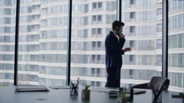 Şirket ofisindeki cep telefonuyla iş görüşmeleri. Zarif iş adamı panoramik pencerenin yanında akıllı telefondan konuşuyor. İşyerinde başarılı bir yönetici cep telefonuyla istemciye danışır.