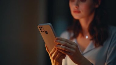 Cep telefonu mesajı okuyan neşeli bir bayan karanlık dairede oturuyor. Gülümseyen iş kadını gece işyerinde akıllı telefona bakıyor. Kadın eli cep telefonu tutuyor. Çevrimiçi iletişim.