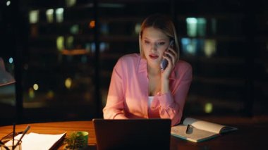 Şirketimizin iş yerinde geç saatlere kadar çalışan gülümseyen sarışın akıllı telefon. Mutlu iş kadını, gece ofisinde dostça cep telefonu sohbetinin tadını çıkarır. Neşeli bayan yönetici telefonda işi tartışıyor.