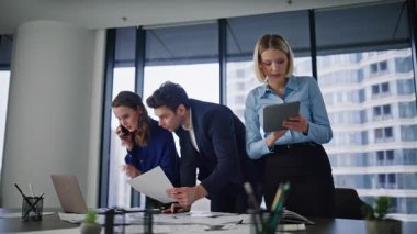 Ofis üyeleri şirket konferans odasında beyin fırtınası yapıyor. İş arkadaşları birlikte proje üzerinde çalışıyor. İş kadını cep telefonunu arıyor. İş adamı kağıtları inceliyor. Tabletteki verileri kontrol eden iş arkadaşı