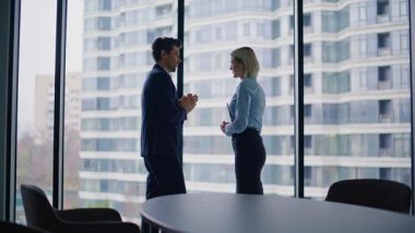 Ofis panoramik penceresinden şirket ortakları konuşuyor. Gülümseyen iş adamları şehir manzarası hakkında tartışıyorlar. İş kadını modern şirket işyerinde birlikte konuşuyor..