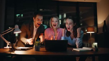 Karanlık ofiste dizüstü bilgisayar arayan iş adamları proje başarısına seviniyor. Aşırı mutlu iş arkadaşları, gece işyerinde beş kişiye sarılıyorlar. Mutlu takım başarılı bir başlangıcın keyfini çıkarın..