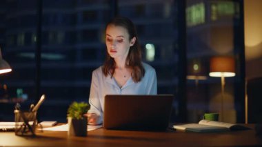 Geç saatlere kadar çalışan bir kadın laptop 'da çalışıyor. Lamba ışığında evrakları kontrol ediyor. Ciddi iş kadını raporları okuyor. Bilgisayardan verileri kontrol ediyor. Çalışkan yönetici ofiste fazla mesai yapıyor.