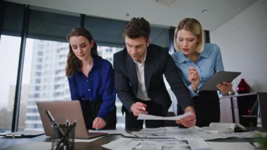 İş ortakları modern ofisteki projeyi analiz ediyorlar. İş kadını, masasında doküman okuyan kendine güvenen iş adamına tablet verilerini gösteriyor. Grup liderleri yoğun toplantıda strateji planlıyor