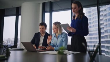 Şirket panoramik ofisinde dizüstü bilgisayardan grup girişimcilerinin videosu. İş yerinde online görüşmeye başlayan üç yönetici webcam 'i selamlıyor. Yaratıcı ajans çalışanları müşterilerine uzaktan danışırlar..