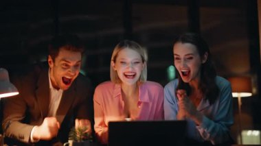 Heyecanlı takım arkadaşları zafere seviniyor. Laptopta harika haberler okuyorlar. Mutlu meslektaşlar iş başarısından çok memnundu. Duygusal partnerler akşam saatlerinde beş takım çalışması yapıyor.