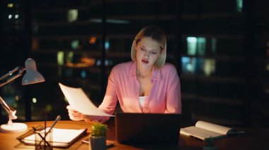 Çalışanlar geç saatlere kadar çalışmaktan memnun değiller. Lamba ışığında belgeleri okuyorlar. Stresli iş kadını, karanlık dizüstü bilgisayar işyerinde mali belgelerde hata buluyor. Endişeli kadın serbest çalışan aşırı yüklenmesi