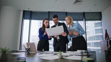 Grup arkadaşları modern konferans odasında proje belgelerini tartışıyorlar. Yaratıcı girişimde işbirliği yapan üç işletme yöneticisi. Grup çalışanları iş yerindeki belgeleri inceliyor..