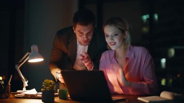 Yaratıcı girişimciler karanlık ajans ofisindeki projede iş birliği yapıyorlar. Tablet memnun takım çalışması verilerini tartışan iş adamlarına ilham kaynağı oldu. Gülümseyen meslektaşlar akşam birlikte çalışıyorlar..