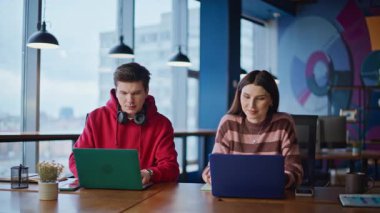 Çevrimiçi çalışan iki bağımsız modern çalışma alanının yakın planında oturuyor. Gülümseyen ofis arkadaşları dizüstü bilgisayar ararken birlikte proje oluşturuyorlar. Arkadaş canlısı ekip içeride e-ticaret girişimini geliştiriyor..